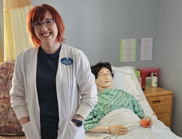 CNA instructor stands in classroom next to skills mannequin